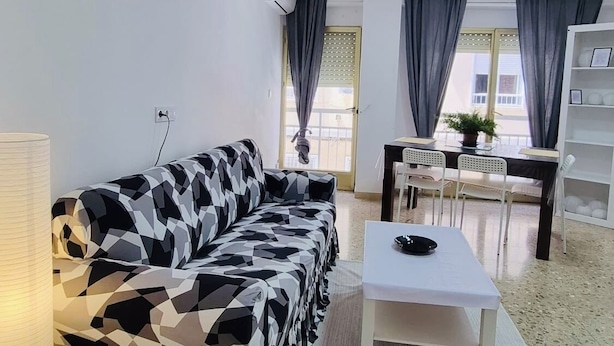 Ett vardagsrum med en soffa, ett soffbord, en lampa och en matplats med stolar och ett bord.