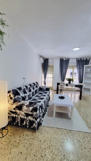 Een woonkamer met een bank, een salontafel, een lamp en een eethoek met stoelen en een tafel.