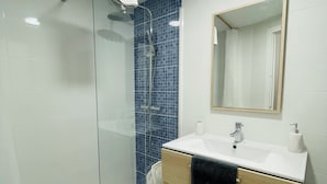 Ett badrum med en dusch som är avskärmad med glasväggar, ett handfat med spegel och en handdukshängare.