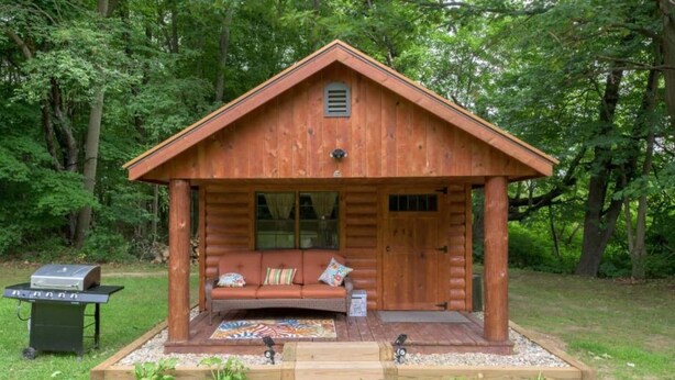 A log cabin with a porch, a grill, and a bench.