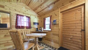 A wooden cabin interior with a round table, chairs, a coffee station, and a door.