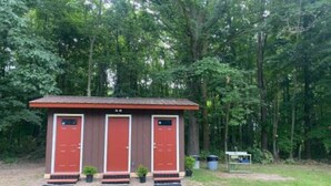 A small, single-story building with three red doors, a metal roof, and a grassy area in front.