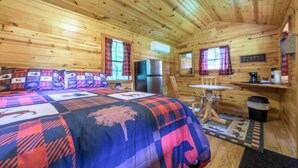 A wooden cabin interior with a bed, a refrigerator, a dining table, and a coffee station.