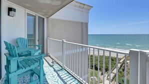 Un balcone con vista sull'oceano, ringhiera bianca e poltrone turchesi.