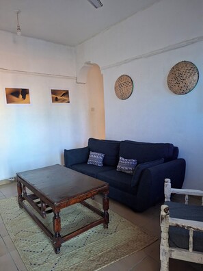A living room with a dark blue sofa, a wooden coffee table, and two wall-mounted woven baskets. - Traditional Swahili Style 1 Bedroom- Bamburi Mombasa (Mombasa)