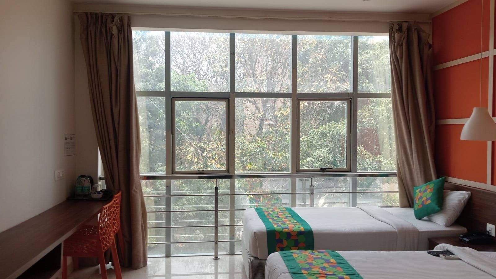 A hotel room with a large window, a desk, two beds, and a chair.