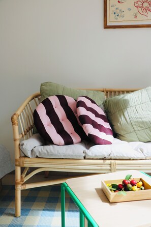 A wicker sofa with striped cushions and a green pillow, a wooden side table with a fruit bowl, and a checkered floor. - Araça Studio - Atlantic Mountain Living Surrounded by mountains and nature (São Vicente)
