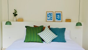 A neatly made bed with pillows, a wall-mounted shelf with decorative items, and a green pendant light. - Araça Studio - Atlantic Mountain Living Surrounded by mountains and nature (São Vicente)