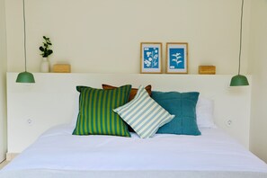 A neatly made bed with pillows, a wall-mounted shelf with decorative items, and a green pendant light. - Araça Studio - Atlantic Mountain Living Surrounded by mountains and nature (São Vicente)