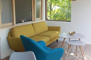 A modern living room with a mustard sofa, a blue armchair, and a small white table with a decorative bowl. - Valomerius - Charming Holiday Home (Maarkedal)
