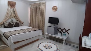 A bedroom with a bed, bedside table, TV, and a small table with bottles. - Orchha Resort- by the river (Nivari)