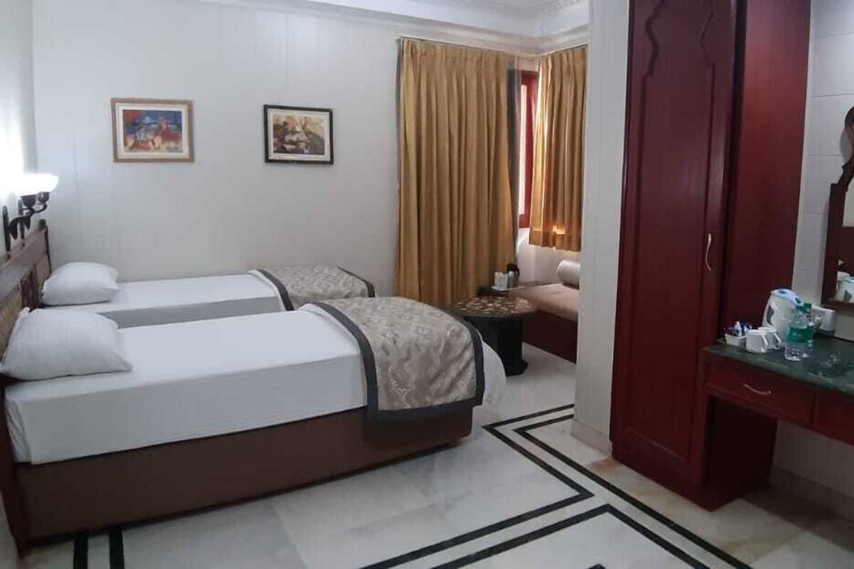 A hotel room with two beds, a sitting area with a sofa, a small table, a mirror, and a window with curtains.
