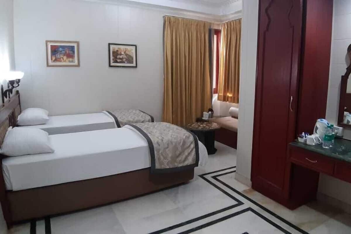 Habitación de hotel con dos camas, zona de estar con un sofá, una mesita y un espejo, además de una ventana con cortinas.