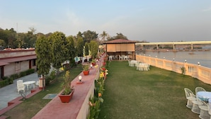 A terrace with outdoor seating, a river view, and a bridge in the background. - Orchha Resort- by the river (Nivari)