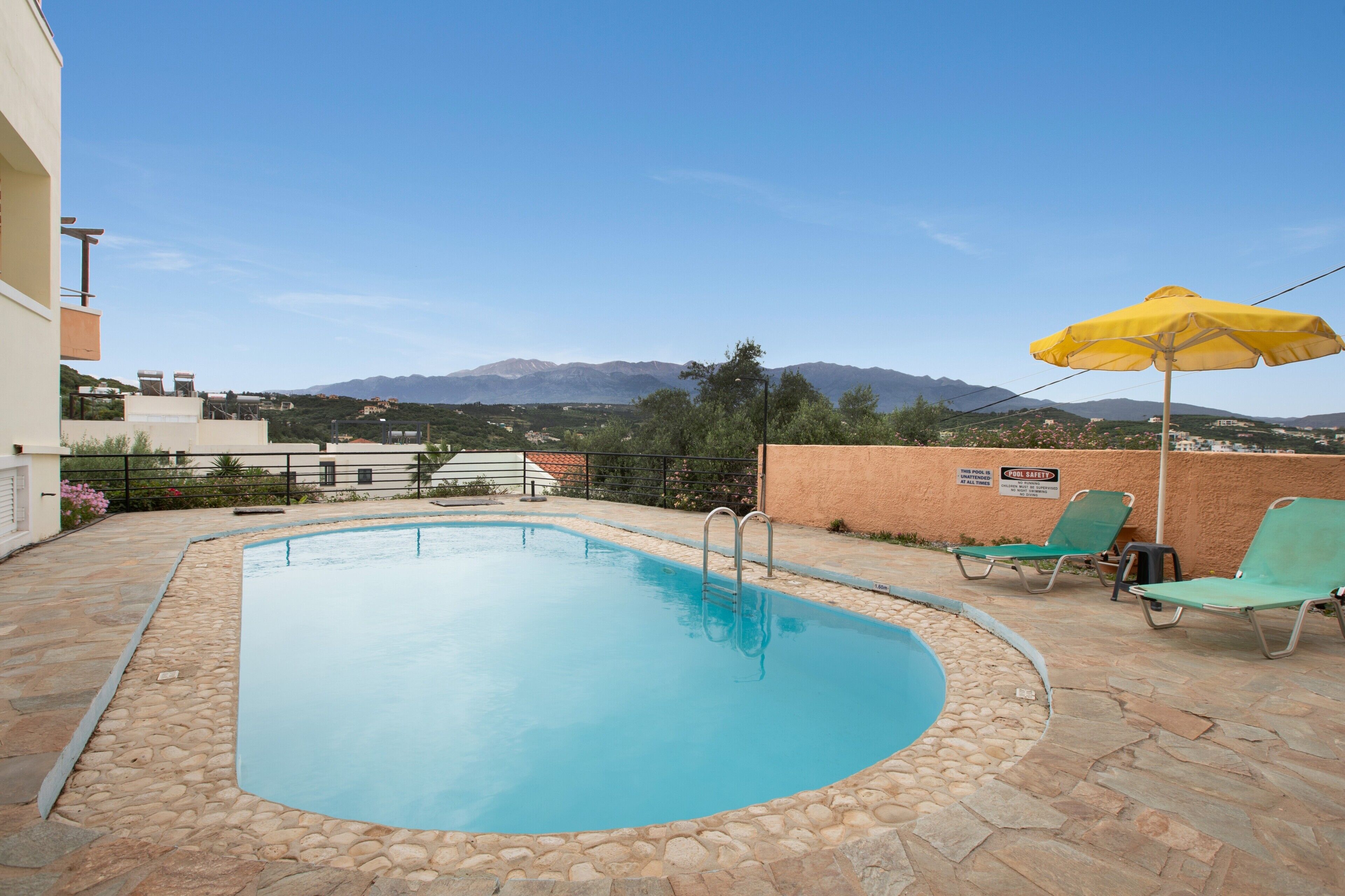 A swimming pool with a stone border, a yellow umbrella, and a view of mountains in the background.