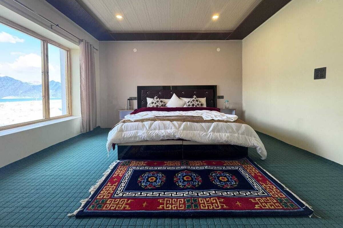 A hotel room with a bed, a window with a view, and a patterned rug.