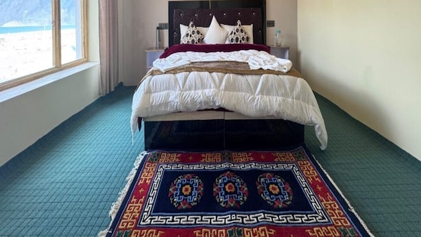A bedroom with a bed, a window with a view of mountains, and a patterned rug.