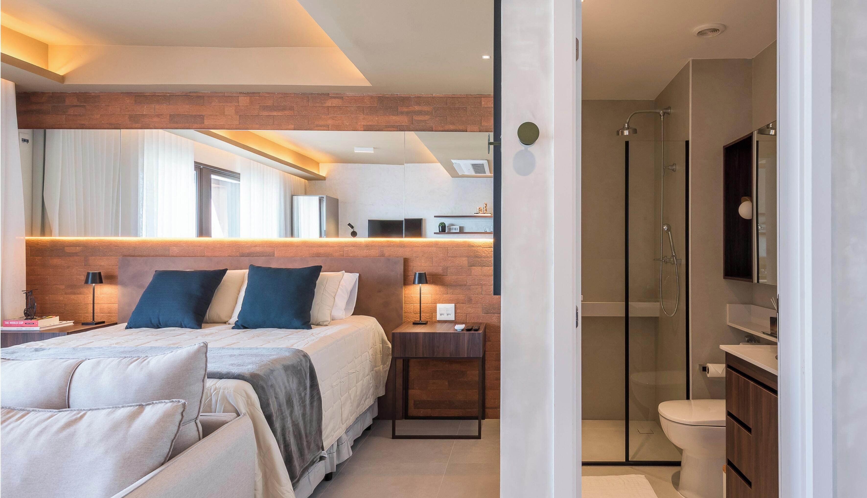 A modern hotel room with a large bed, bedside tables, a TV, and a separate bathroom with a shower and toilet.
