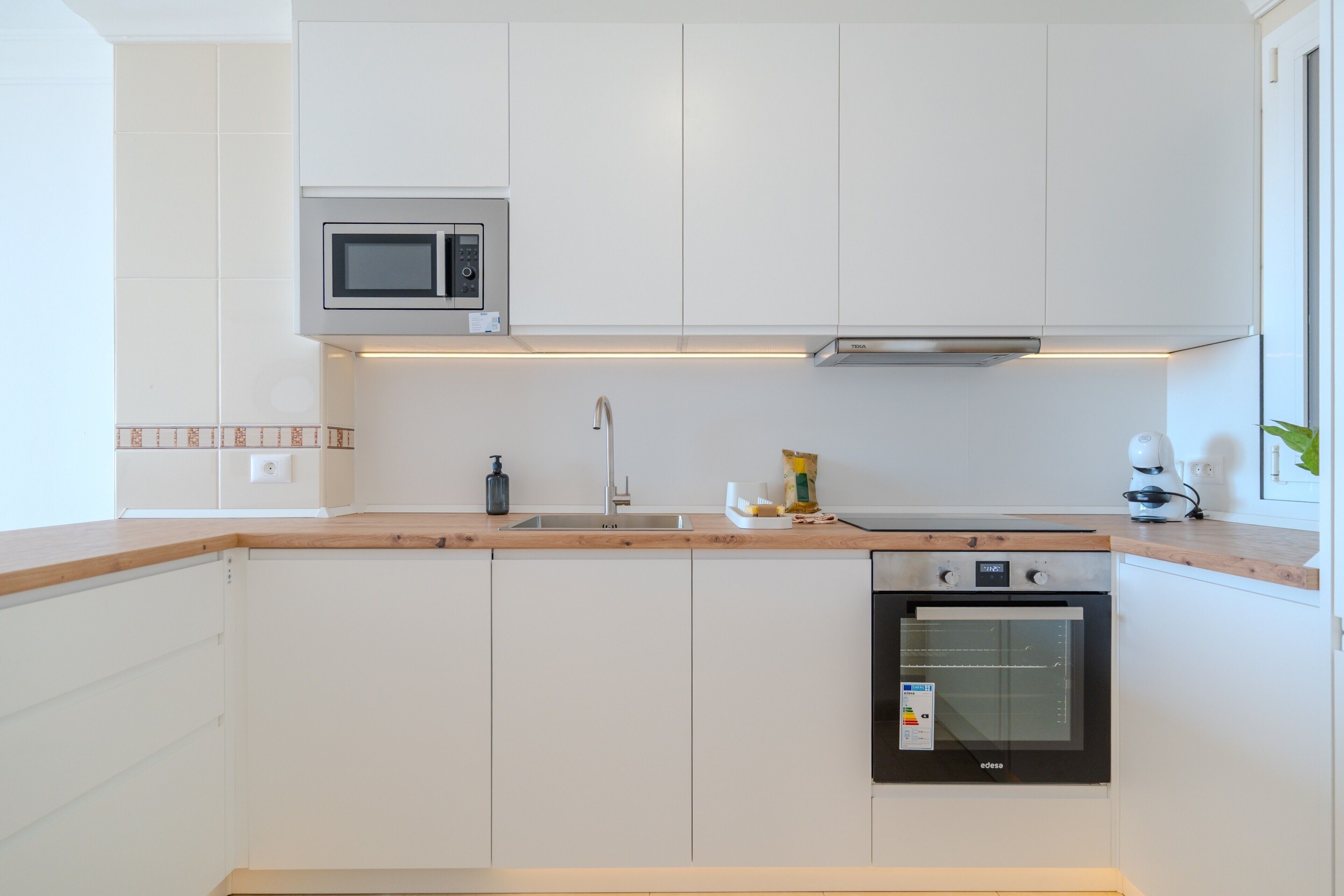 A modern kitchen with white cabinets, a microwave, a sink, a stove, and a toaster.