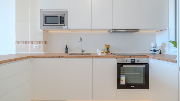 Una cocina moderna con armarios blancos, microondas, fregadero, estufa y tostadora.