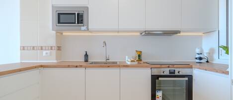 A modern kitchen with white cabinets, a microwave, a sink, a stove, and a toaster.