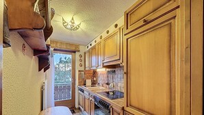 A kitchen with wooden cabinets, a stove, and a window overlooking greenery. - A living room with dining area and fireplace, a separate kitchen with dishwasher, a double bedroom, (Verbier)