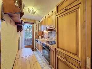 A kitchen with wooden cabinets, a stove, and a window overlooking greenery. - A living room with dining area and fireplace, a separate kitchen with dishwasher, a double bedroom, (Verbier)