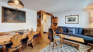 A cozy living room with a dining area, a blue sofa, wooden furniture, and a patterned rug. - A living room with dining area and fireplace, a separate kitchen with dishwasher, a double bedroom, (Verbier)