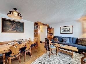 A cozy living room with a dining area, a blue sofa, wooden furniture, and a patterned rug. - A living room with dining area and fireplace, a separate kitchen with dishwasher, a double bedroom, (Verbier)