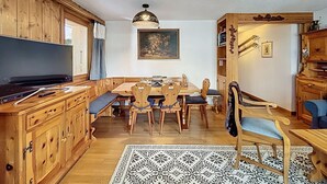 A wooden interior with a dining table, chairs, a television, and a patterned rug. - A living room with dining area and fireplace, a separate kitchen with dishwasher, a double bedroom, (Verbier)