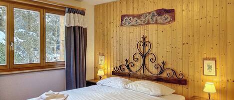 Un dormitorio con una cama, dos mesitas de noche, un ventanal con cortinas y una pared de madera con un panel decorativo.