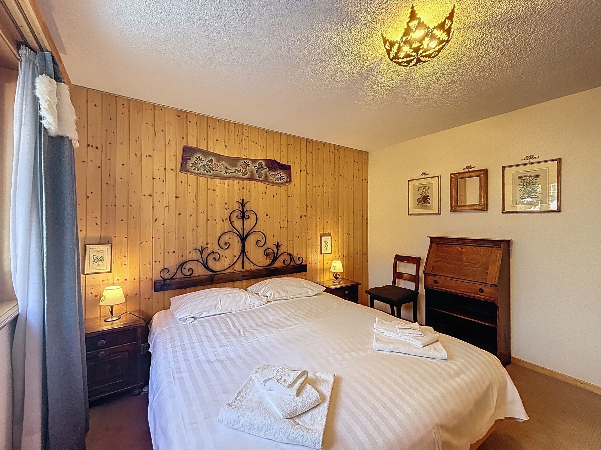 Ein Hotelzimmer mit einem hölzernen Kopfteil, einem Bett mit weißen Leinen, zwei Nachttischlampen, einer Holzkommode und gerahmten Bildern an der Wand.