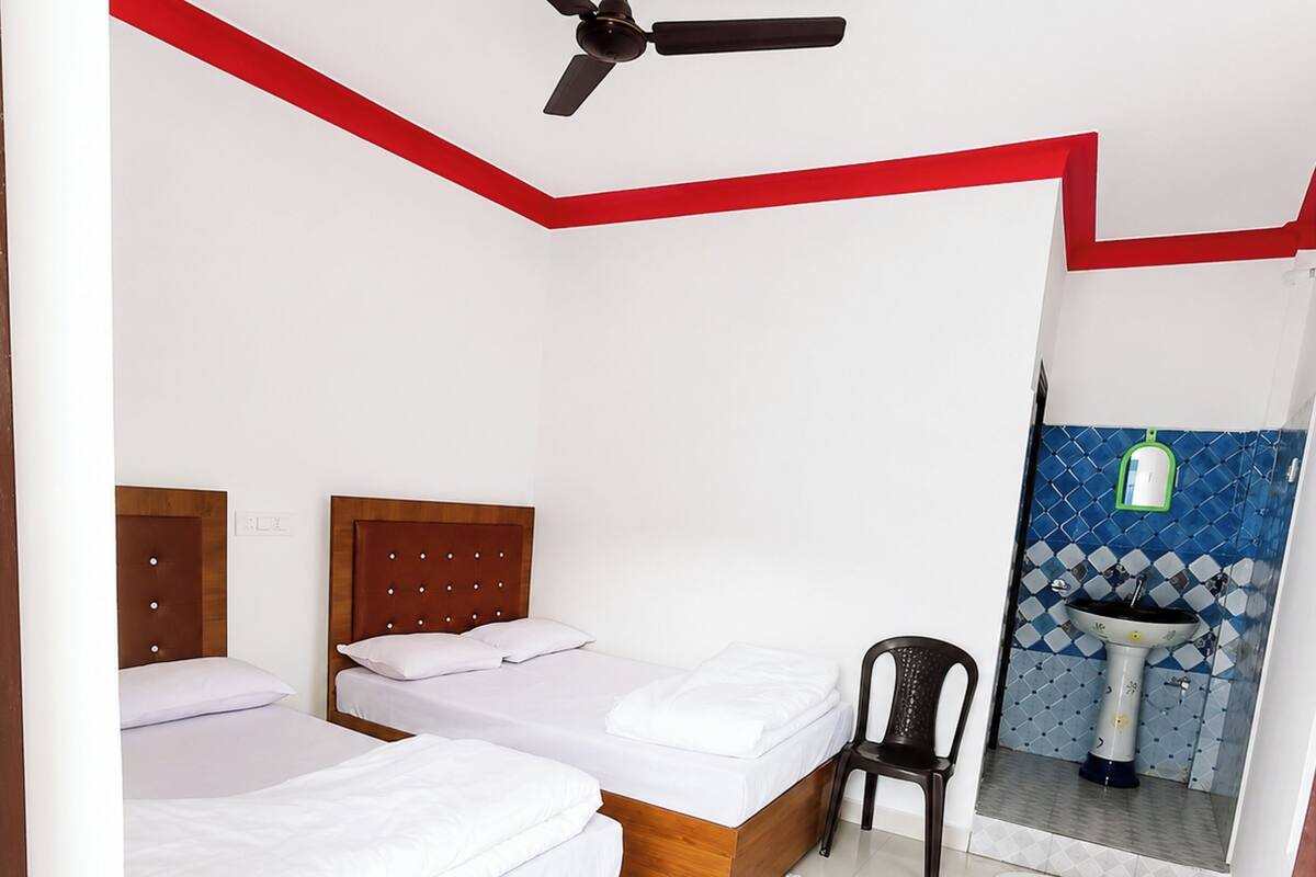 A bedroom with two beds, a ceiling fan, a chair, and a bathroom visible through an open door.