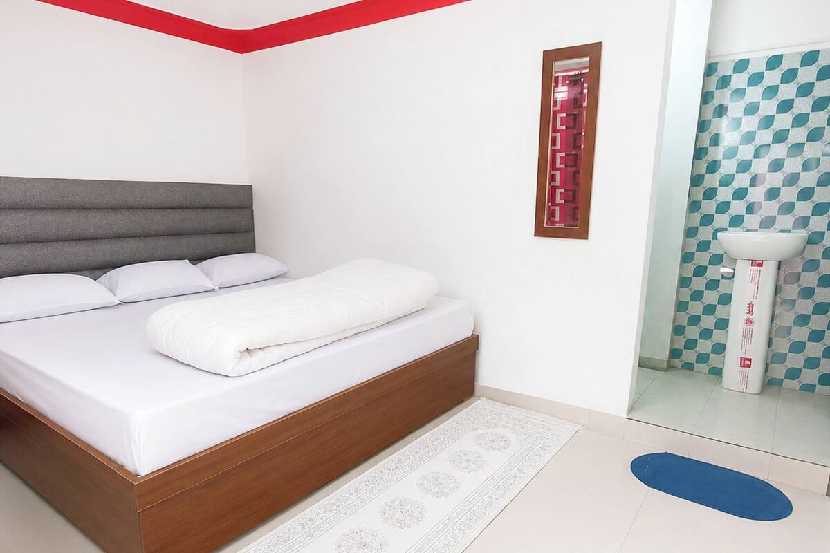 A modern bedroom with a bed, a bedside table, a mirror, and a bathroom with a sink and toilet.