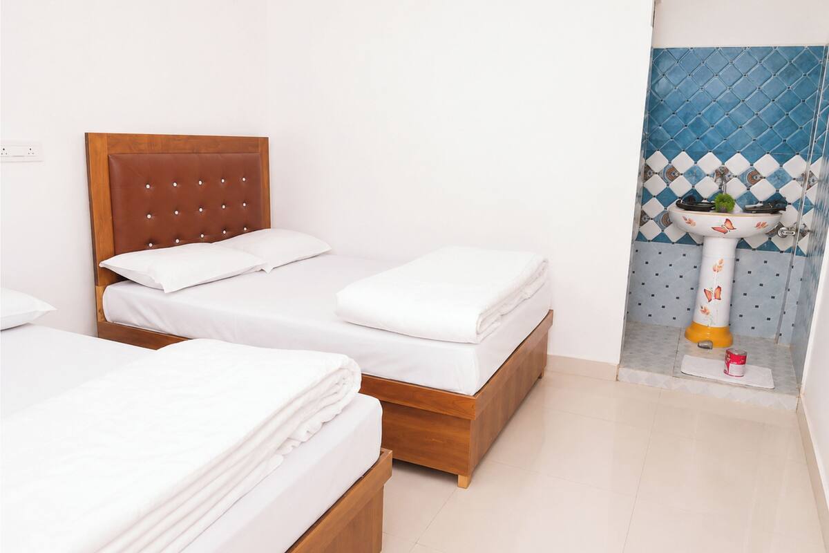 A hotel room with two wooden beds, white bedding, a bathroom with a sink and decorative tiles.
