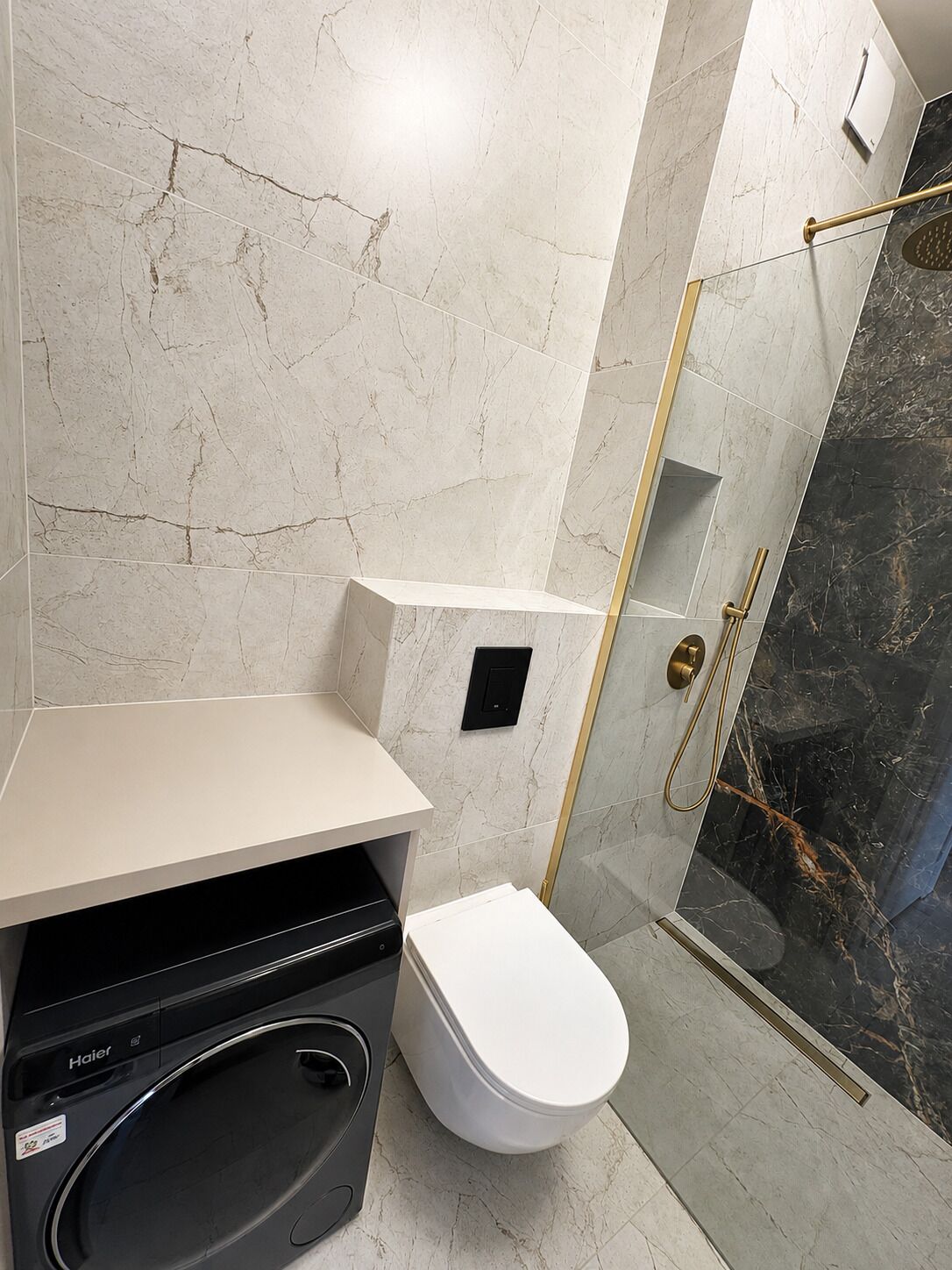 A bathroom with a white toilet, a black washing machine, and a glass-enclosed shower area.