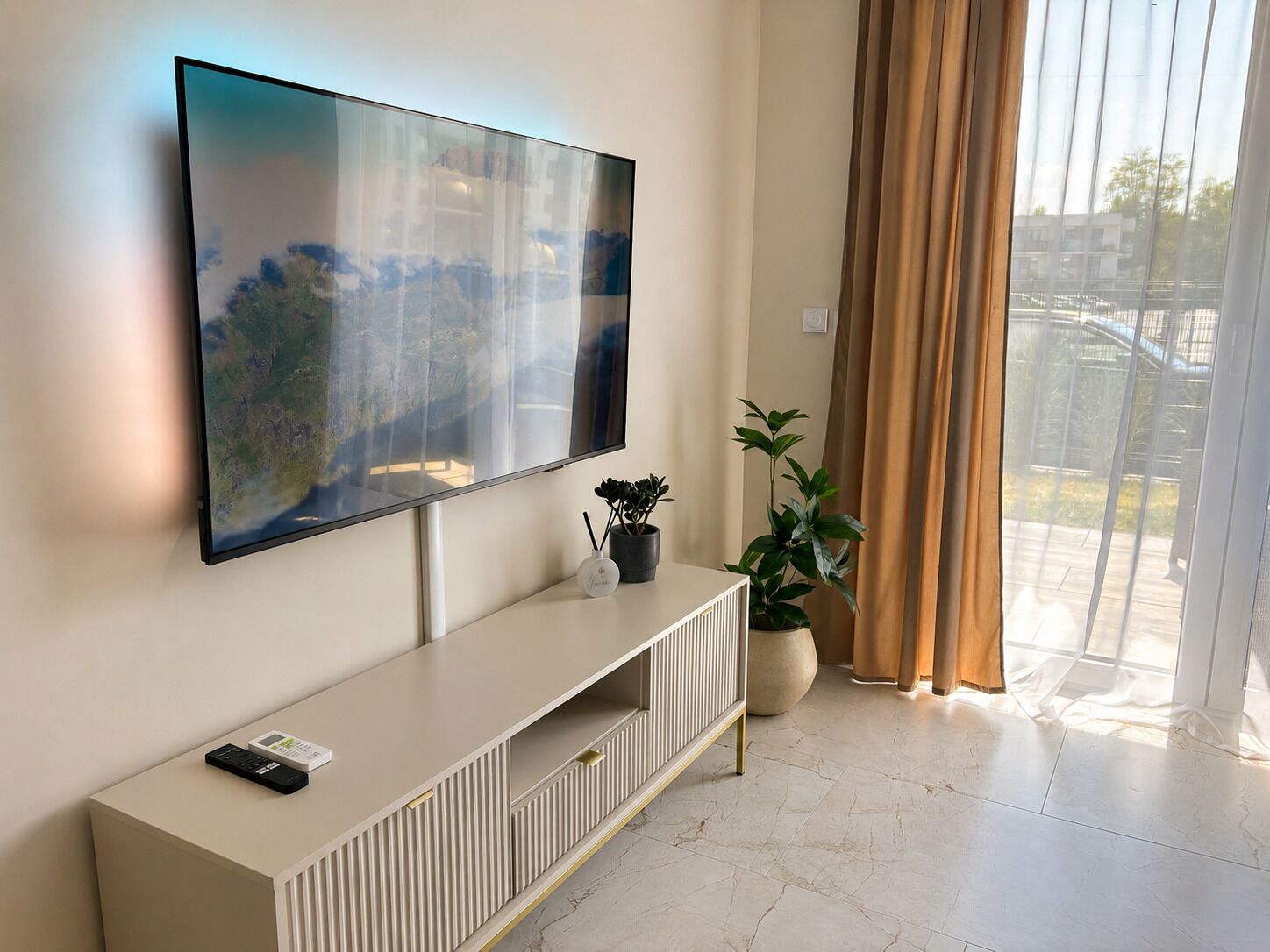 Una sala de estar moderna con un televisor de pantalla plana grande montado en la pared, una consola blanca con un control remoto y una planta en maceta.