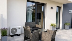 Un espace extérieur moderne aménagé avec des meubles en osier, une table en verre et des plantes en pot.