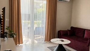 Un salon moderne avec un canapé, une table basse, un téléviseur et une grande fenêtre avec des rideaux.