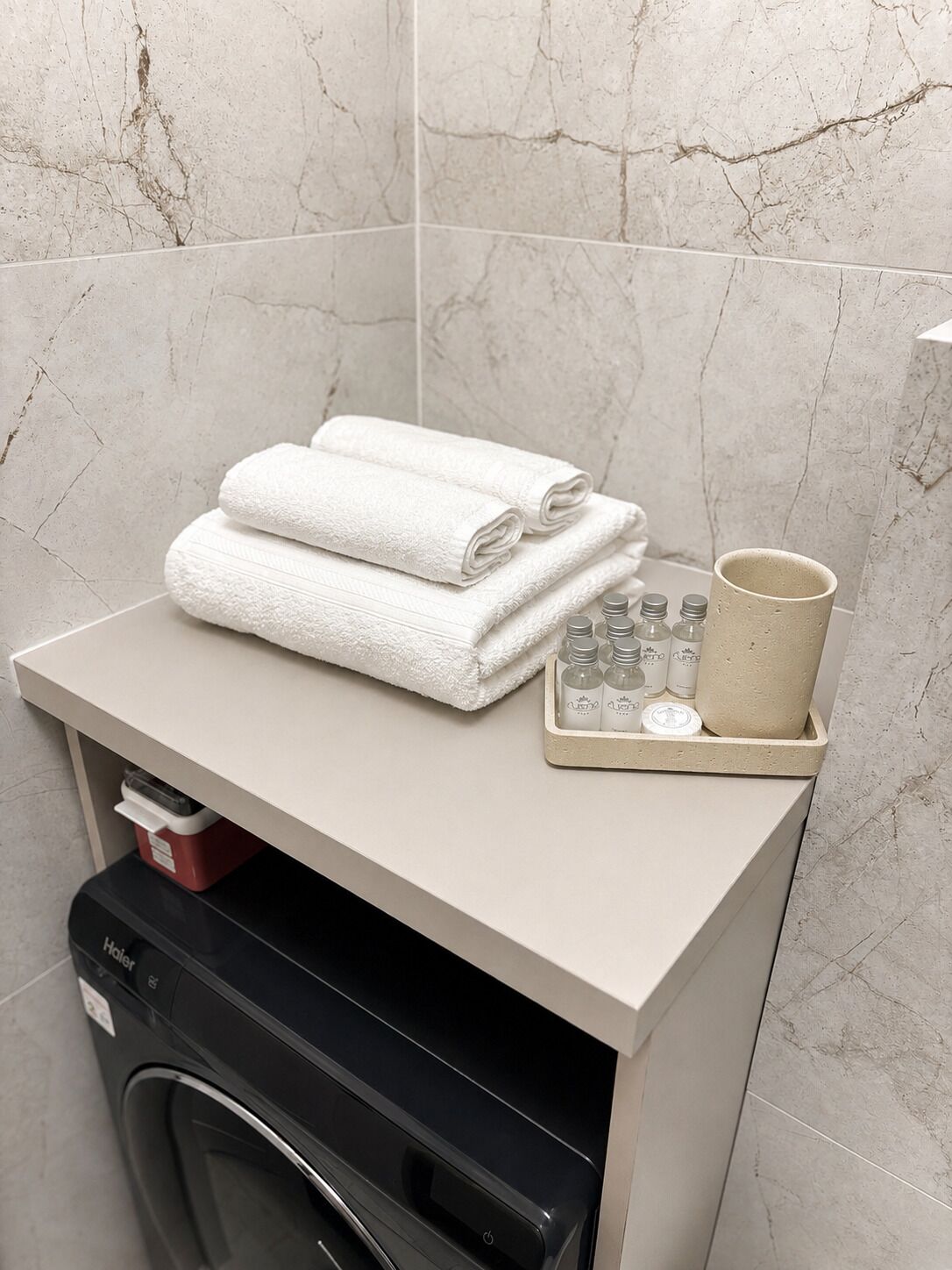 A bathroom with a towel rack, a cup, and a soap dispenser on a shelf.