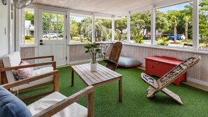Quarto com teto de madeira, porta branca, mesa de madeira, uma cadeira, um armário vermelho e vista para o exterior.