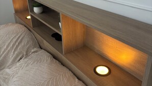 Un dormitorio con una cama, una mesita de noche, una estantería con una planta y una pared decorada con un mural botánico.