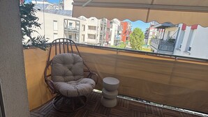 Un balcón con piso de madera, una silla acolchada, una mesita y un dosel.
