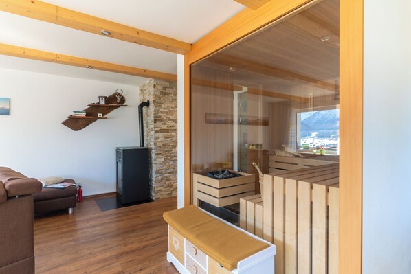A modern living room with a sofa, a wooden bench, a fireplace, and a view of a mountain. - Panoramic Mountain Views, Spacious Sauna, Dogs Welcome, Alpenjuwel 2 Oberstdorf (Oberstdorf)