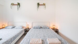 Dos camas individuales con ropa de cama estampada, mesitas de noche con lámparas y plantas colgantes en las paredes.