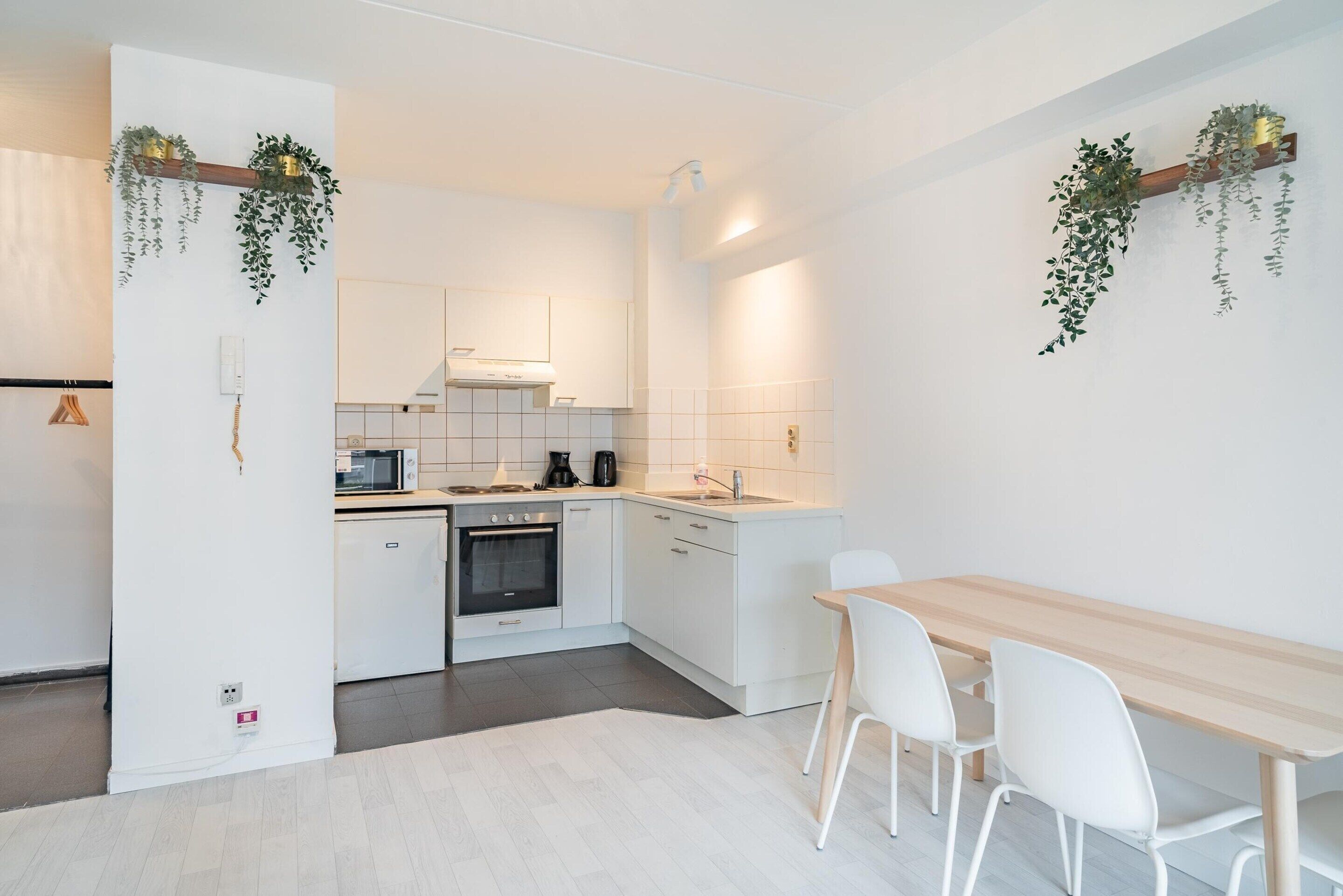 Een moderne keuken met witte kastjes, een houten eettafel en hangende planten.