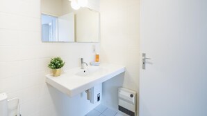 Un baño blanco con lavamanos, espejo y una pequeña planta en maceta.