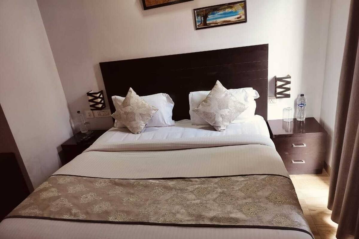 A hotel room with a large bed, a headboard, a bedside table with a lamp, and a nightstand with a bottle.