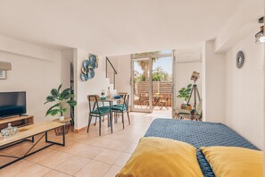 Ein modernes Schlafzimmer mit Bett, Fernseher, Essbereich mit Stühlen und Tisch sowie einer Schiebetür zu einer Terrasse.