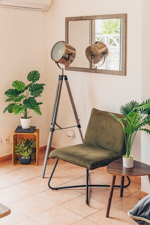 A room with a green chair, a tripod floor lamp, a potted plant, and a window with a view of a deck. - Apartment Le nid D'Azur by Sur la mer (Mandelieu-la-Napoule)